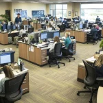 Vaste plateau de bureaux où des équipes travaillent sur des postes à plusieurs écrans