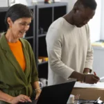 Commerçante sur un ordinateur portable à côté d'un collègue qui annote un colis