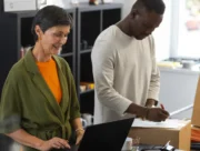 Commerçante sur un ordinateur portable à côté d'un collègue qui annote un colis