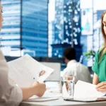 Entretien de recrutement : deux femmes examinent un CV et des documents à une table de bureau