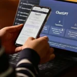 Personne consultant ChatGPT sur un smartphone devant un ordinateur portable