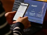 Personne consultant ChatGPT sur un smartphone devant un ordinateur portable