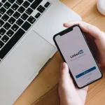 Smartphone affichant l'écran d'accueil de LinkedIn à côté d'un ordinateur portable