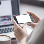 Personne tenant un smartphone à l’horizontale devant un ordinateur portable, illustration du vol de données par photo d’écran en centre d’appels