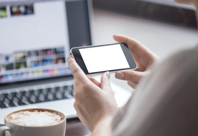 Personne tenant un smartphone à l’horizontale devant un ordinateur portable, illustration du vol de données par photo d’écran en centre d’appels